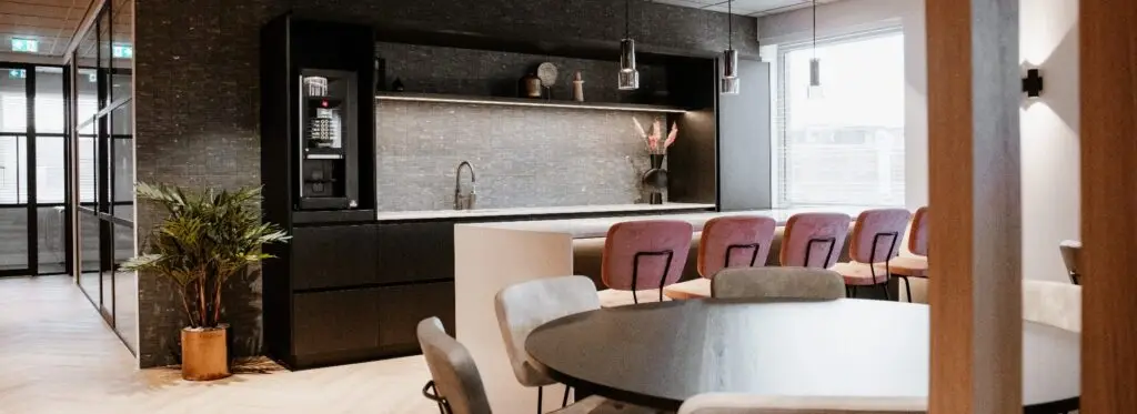 Impressie van een keuken in een kantoorpand, waarbij de wanden voorzien zijn van keramische natuursteenlook tegels in een warme tint, wat fraai contrasteert met de lichte vloer.