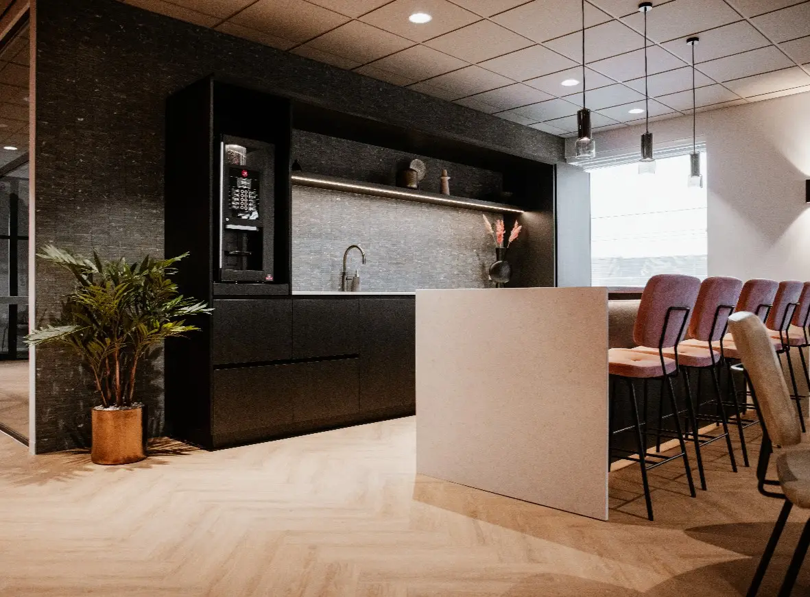 Impressie van een keuken in een kantoorpand, waarbij de wanden voorzien zijn van keramische natuursteenlook tegels in een warme tint, wat fraai contrasteert met de lichte vloer.