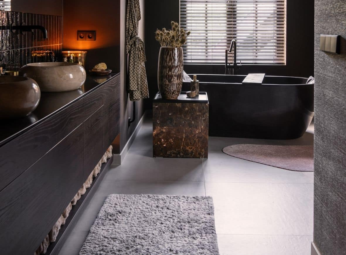 Impressie van een badkamer met grote vloertegels in grijs. Bij het badkamermeubel zien we een accentwand van glanzende zwarte tegels, die verticaal geplaatst zijn.