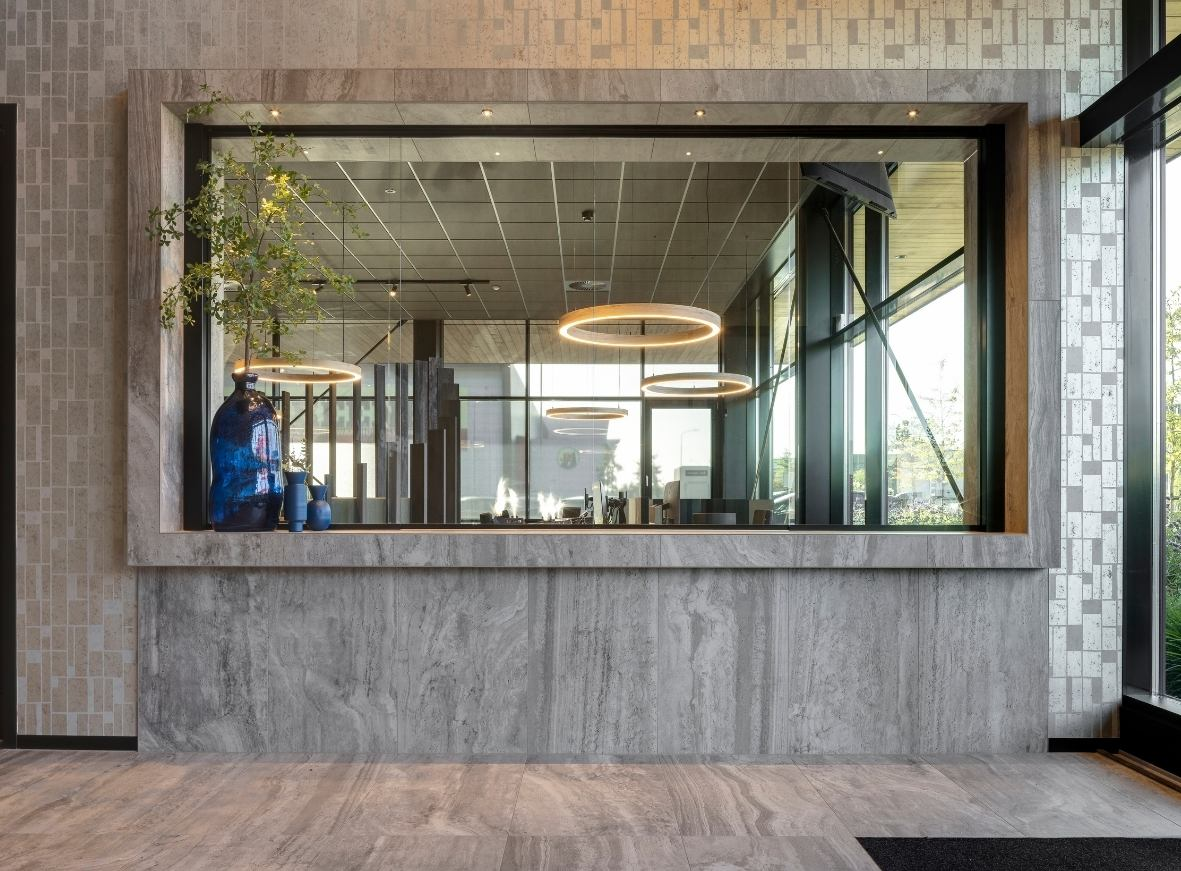 Impressie van een entree van een kantoorpand, voorzien van een grijze gerectificeerde keramische tegel als loket omlijsting.