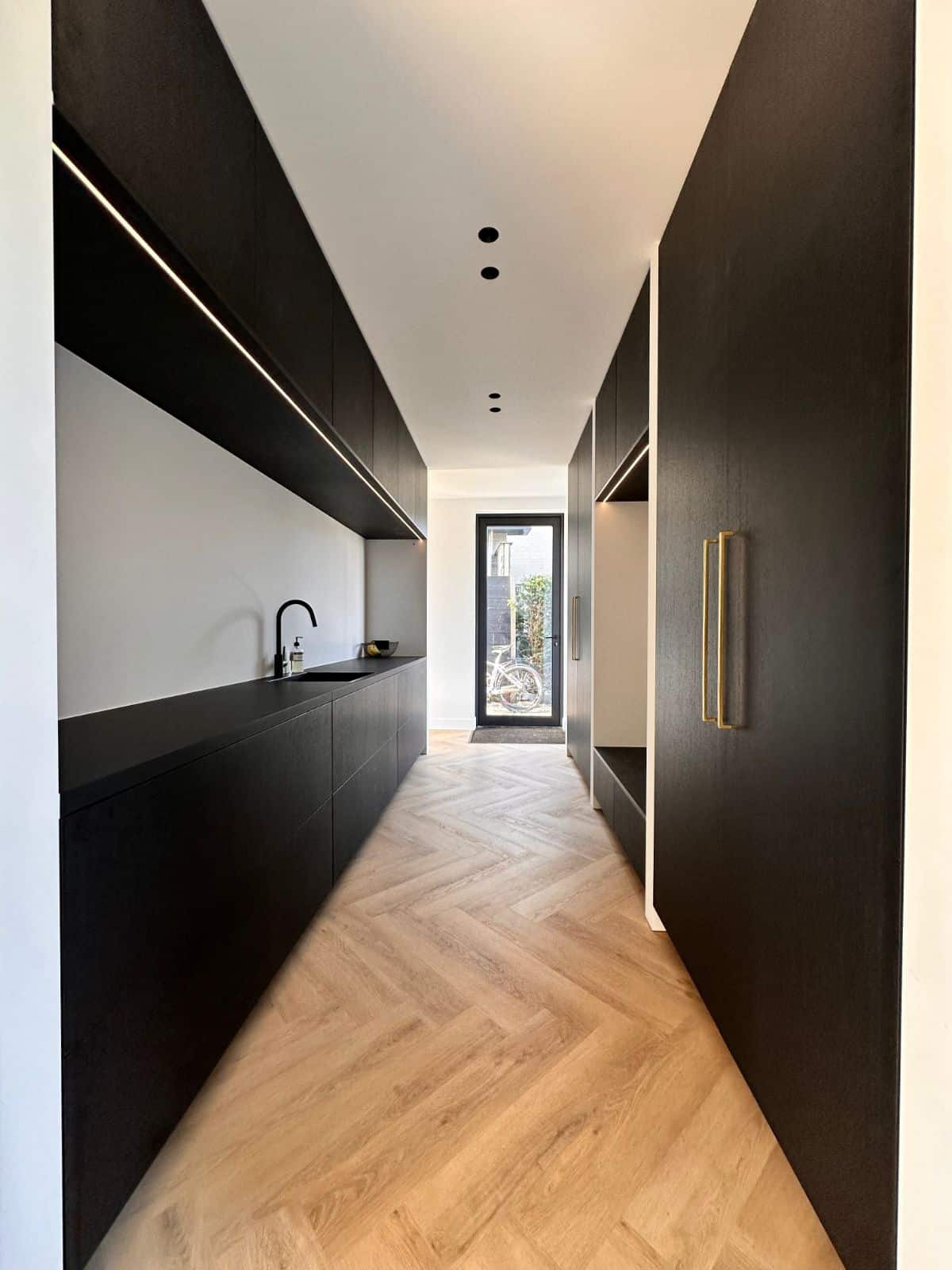 Hal met visgraat pvc vloer en zwarte kasten met nis en aanrechtblad