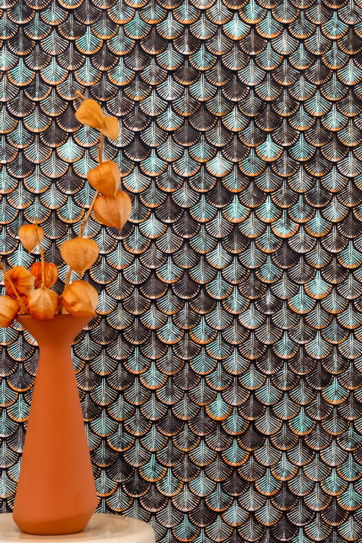 Een close-up van een wand met tegels die een patroon van gestileerde veren in blauw- en goudtinten vormen, met een decoratief effect dat een levendige, artistieke uitstraling geeft.