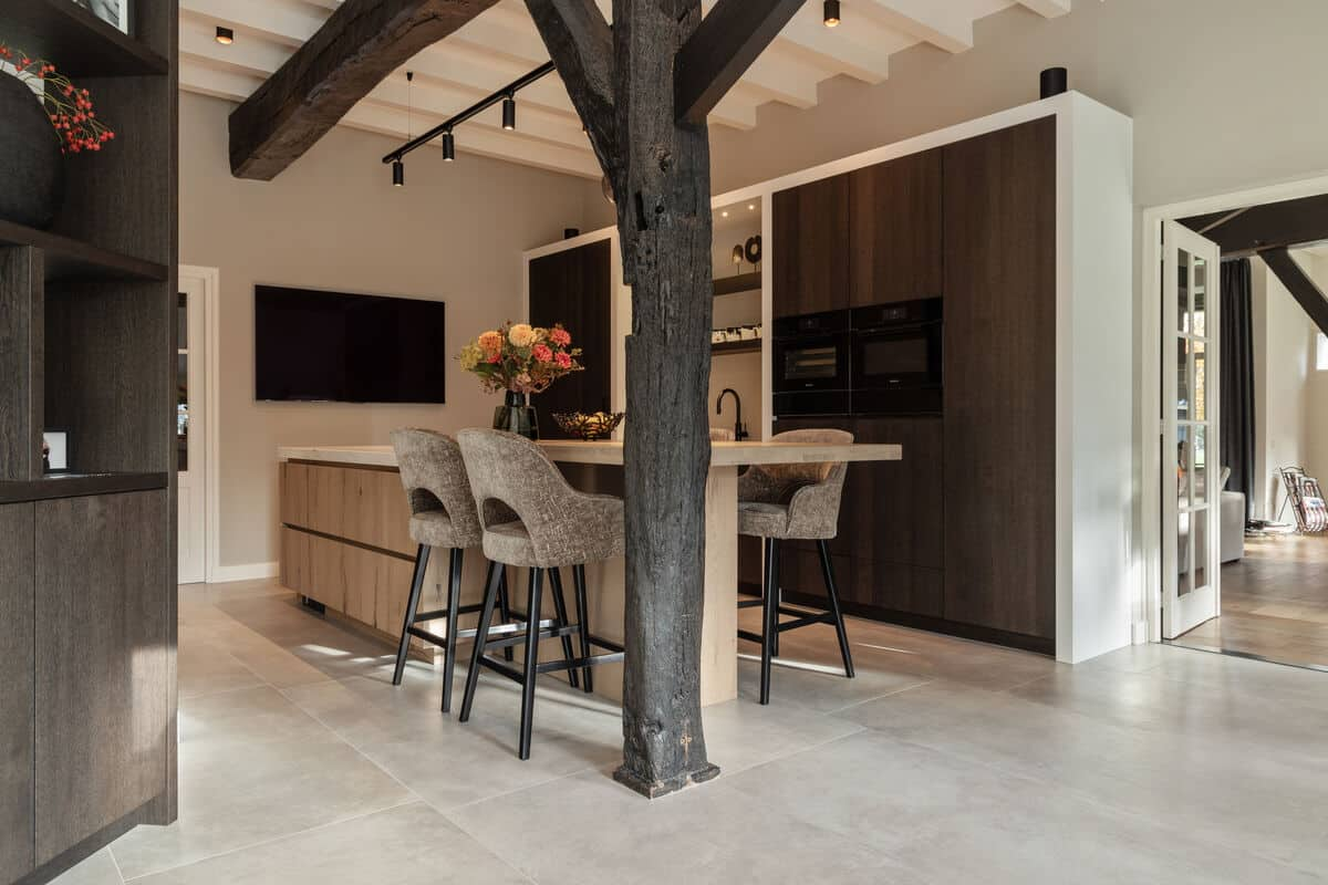 Moderne keuken met donkere houten kasten, een kookeiland, zwarte balken en een landelijke vloer van lichte tegels.