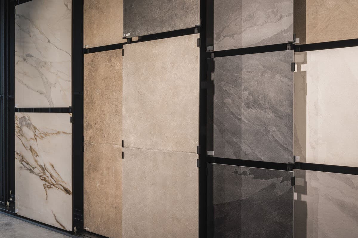 Tegl showroom met diverse landelijke vloertegels in verschillende kleuren en texturen, waaronder marmer, beige en grijze tinten, aan wandpanelen.