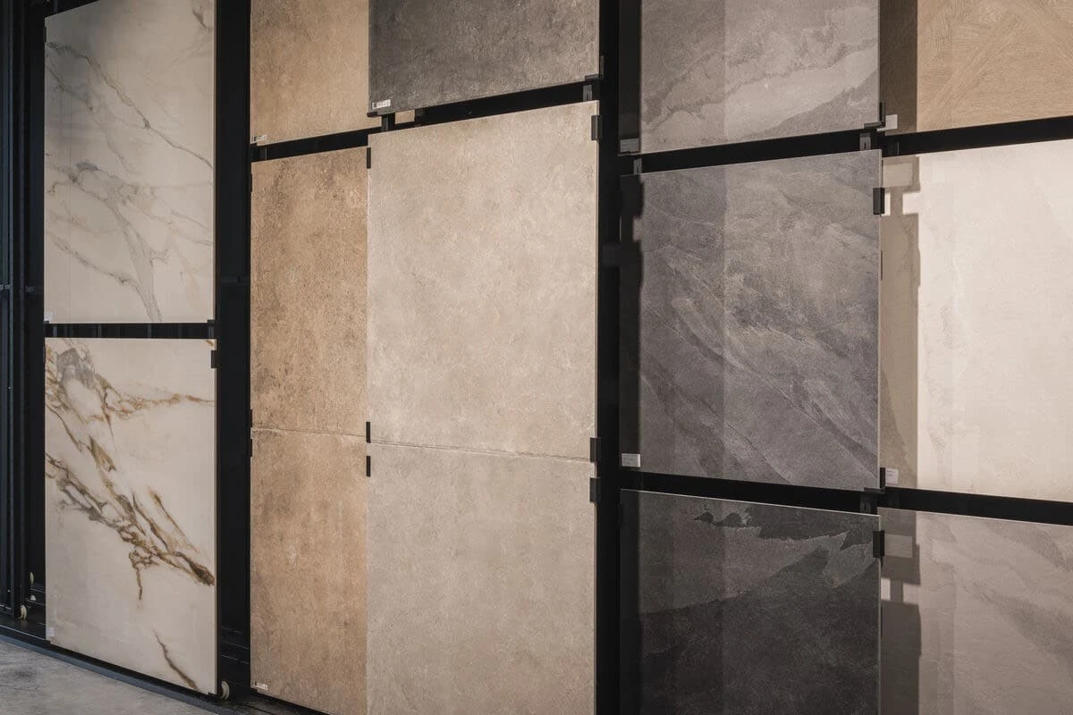 Tegl showroom met diverse landelijke vloertegels in verschillende kleuren en texturen, waaronder marmer, beige en grijze tinten, aan wandpanelen.