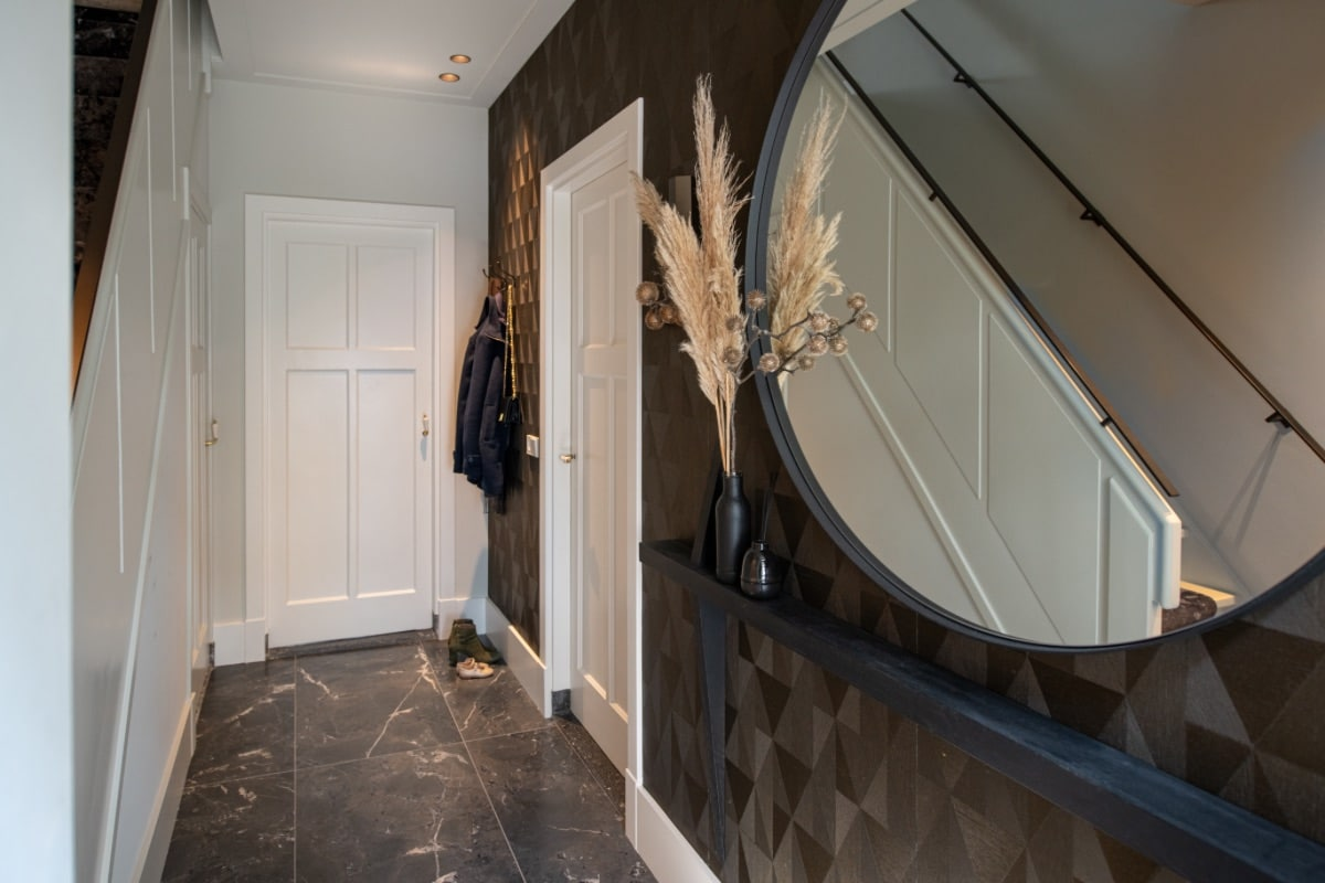 Entree van een moderne hal met geometrisch behang, een ronde spiegel en zwarte accenten, wat een chique uitstraling geeft.