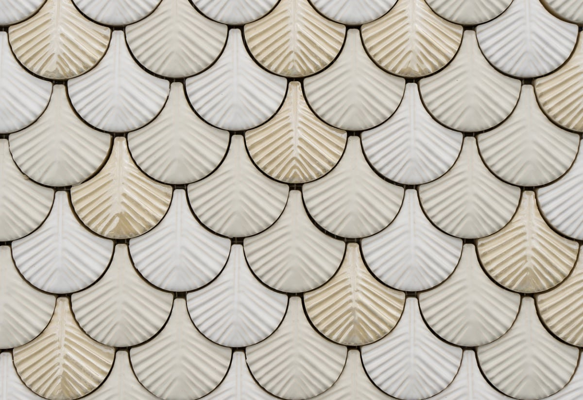 Een gedetailleerde close-up van witte en beige tegels met een schubachtig patroon, waarbij de tegels licht reflecteren en een zacht visueel effect creëren.