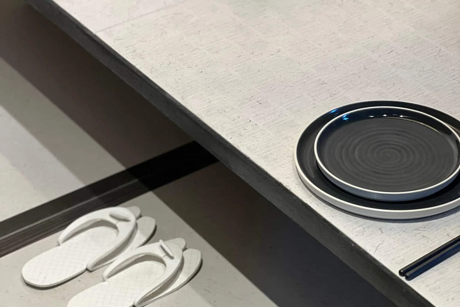 De afbeelding toont een Japandi-geïnspireerd interieur met een minimalistisch ontwerp. Een lichtgekleurde, subtiele tafel is voorzien van een zwart-wit gestreept bord en eetstokjes.