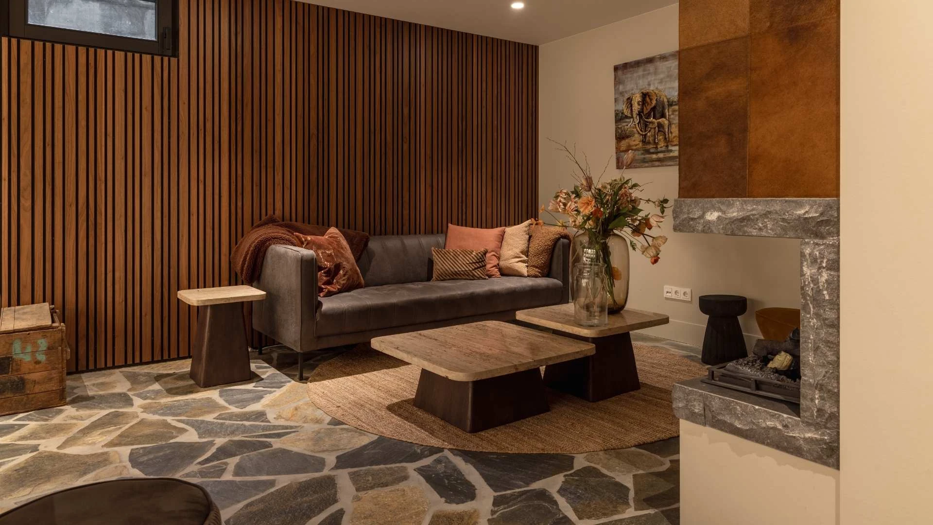 Impressie van een landelijk ingerichte zithoek, met een vloer van blue flagstones, lederen bank, salontafels met marmeren blad, open haard en lattenwanden in hout.