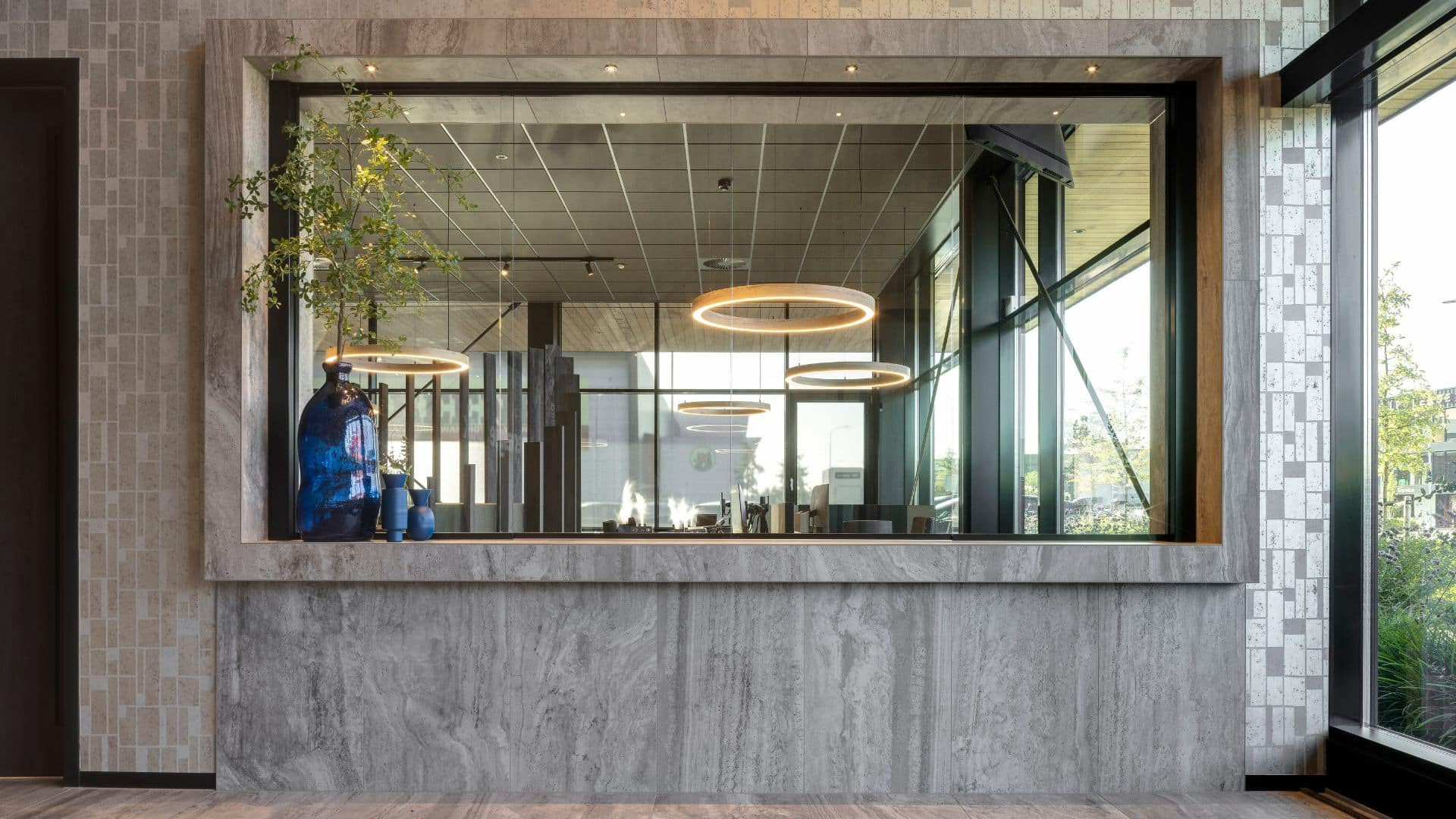 Impressie van de entree van een kantoorpand, voorzien van een grijze keramische tegel als balie omlijsting. De tegel heeft een travertin uitstraling.